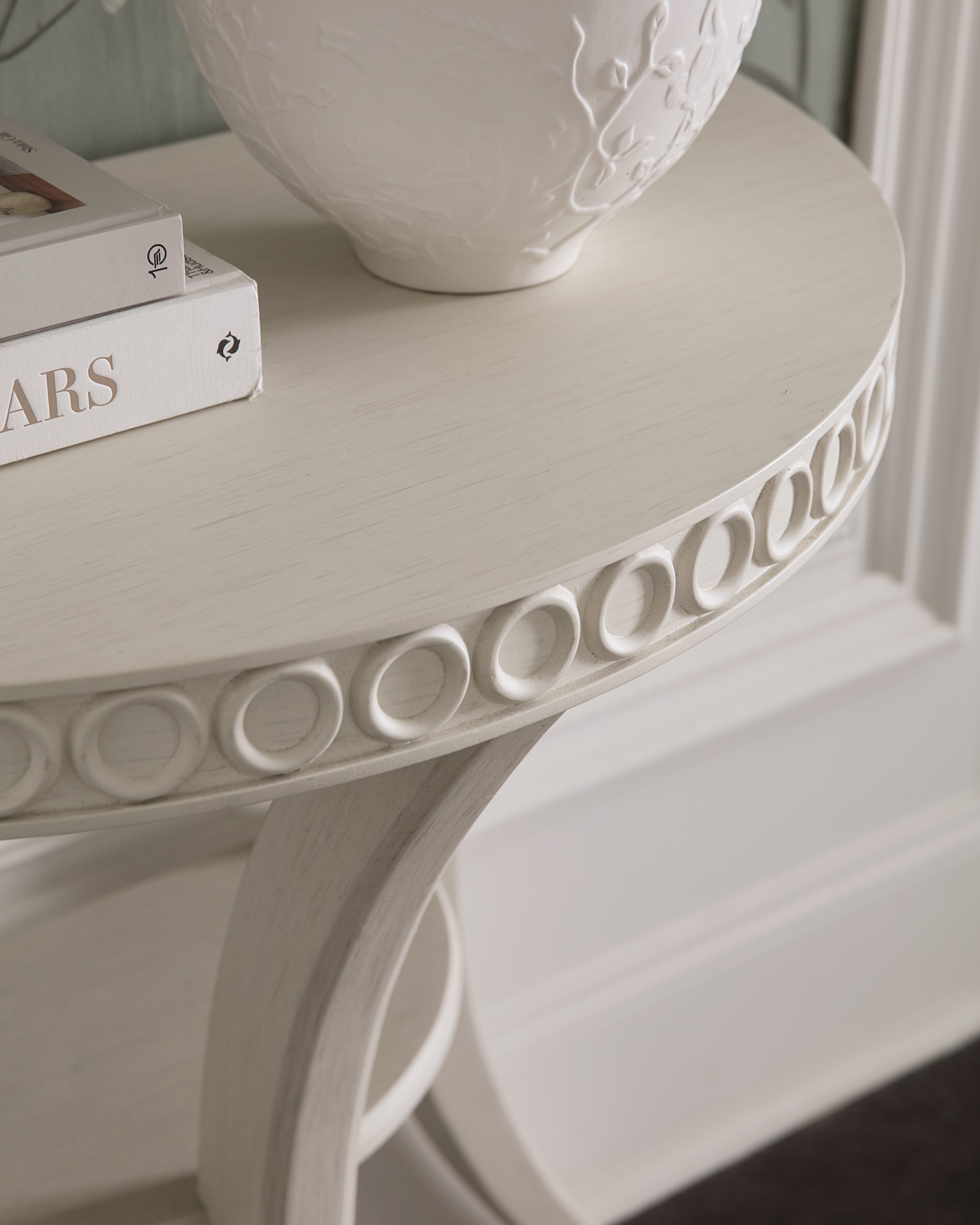 Round decorative table with intricate carvings and a white vase on top.