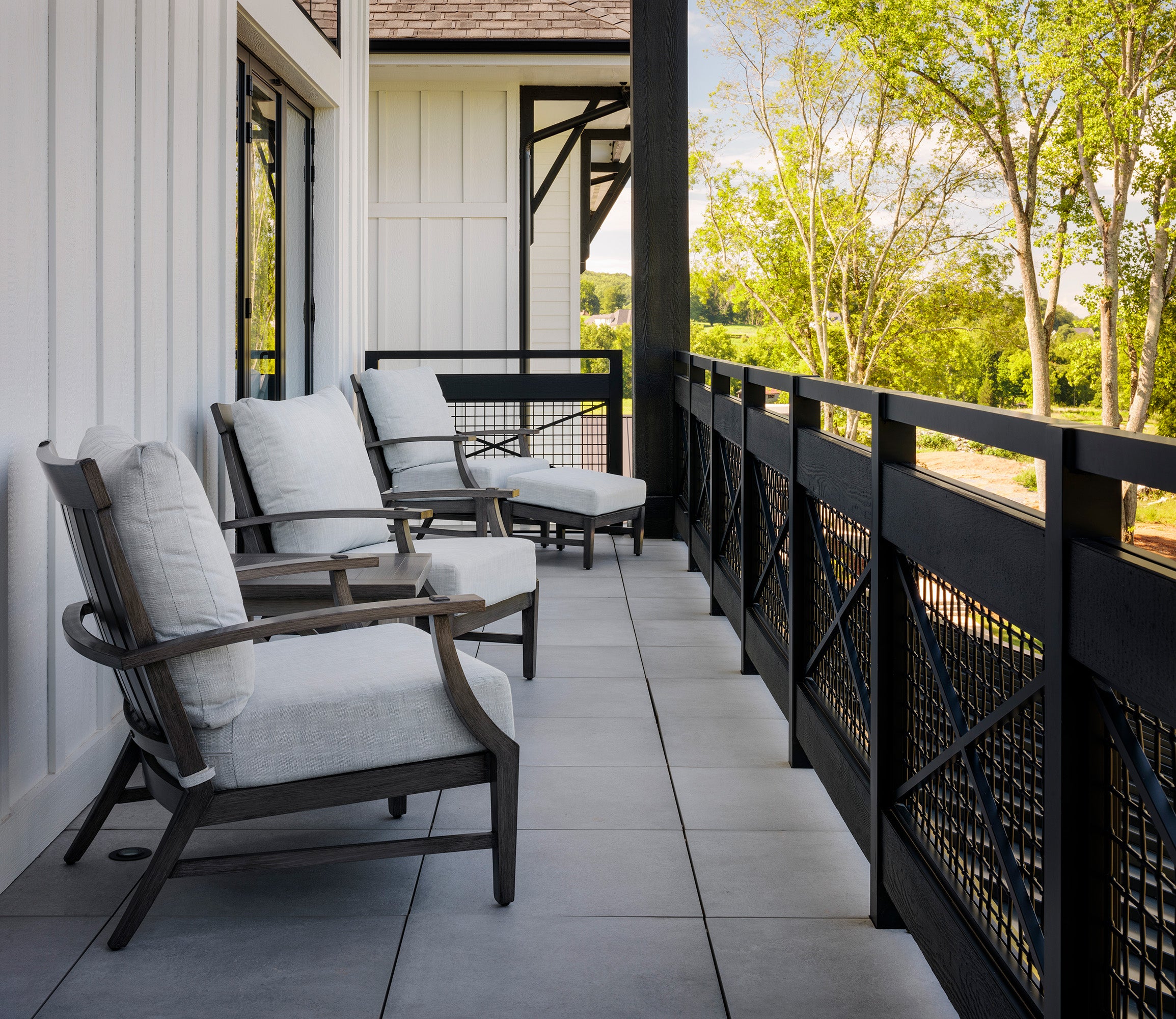 Outdoor patio with aluminum chairs and a railing overlooking trees.