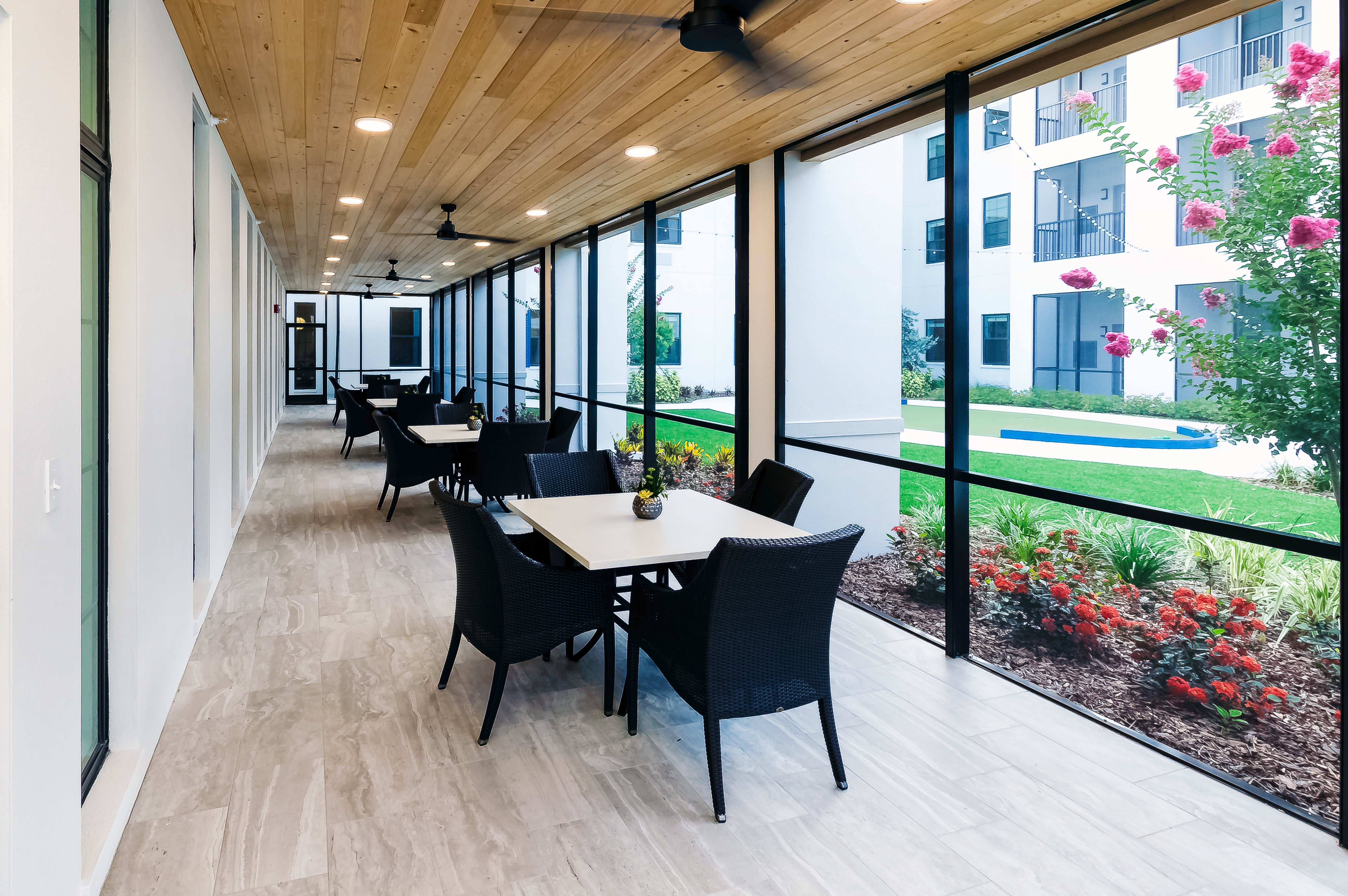 Modern office interior with tables and chairs by large windows overlooking a garden.