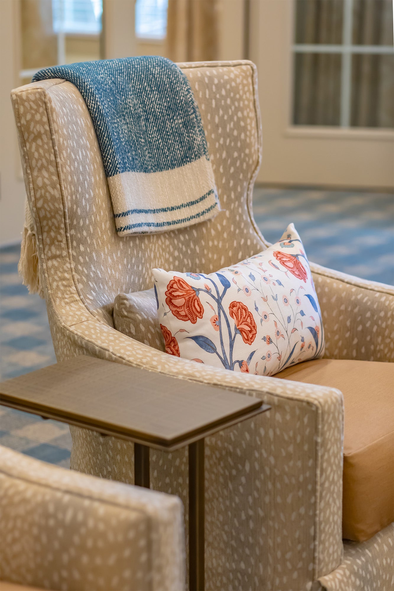 Beige armchair with a blue and white towel draped over it and a floral pillow in a room with a checkered floor.
