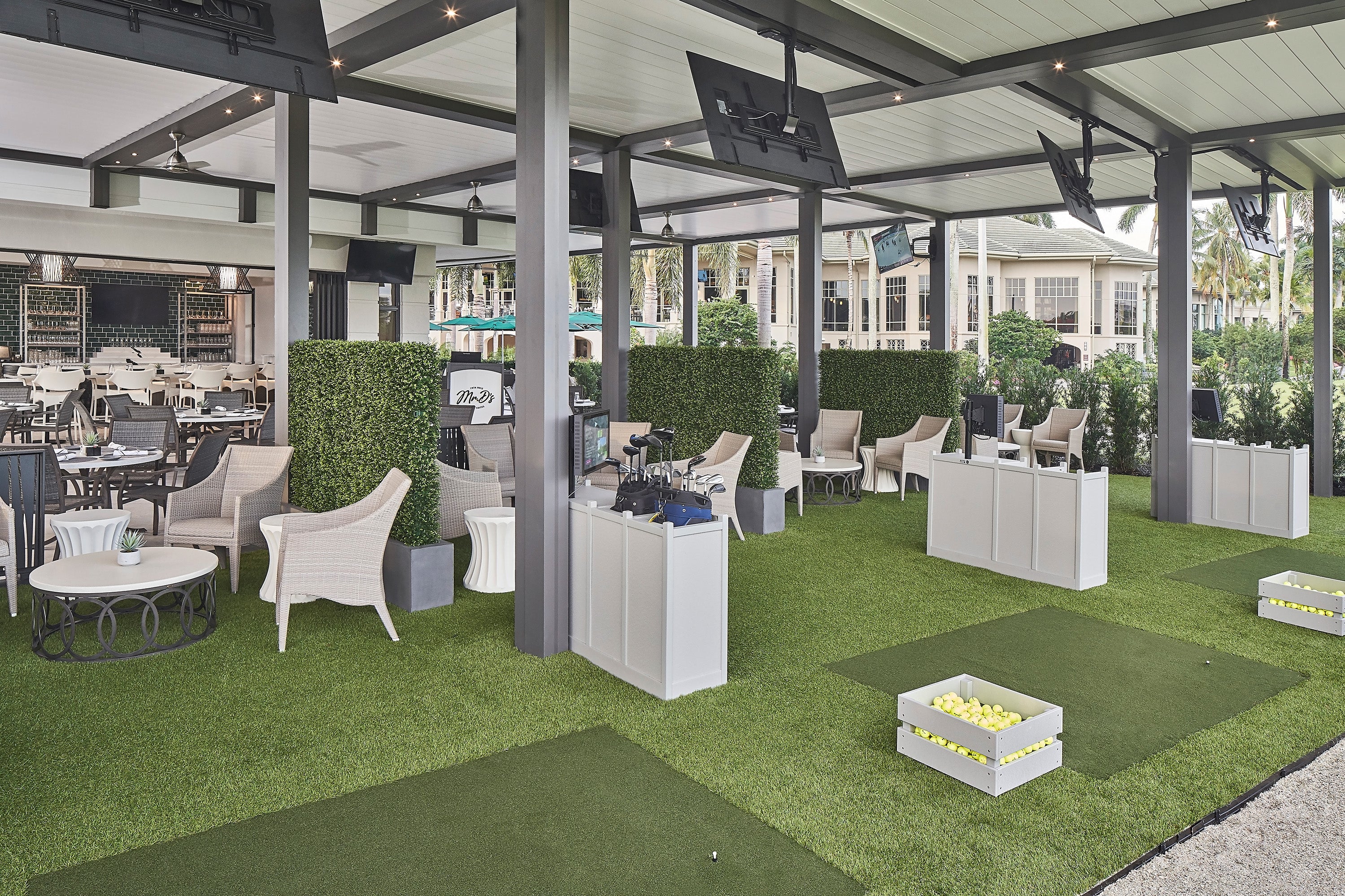 Indoor golf simulator area with green turf, chairs, and screens.