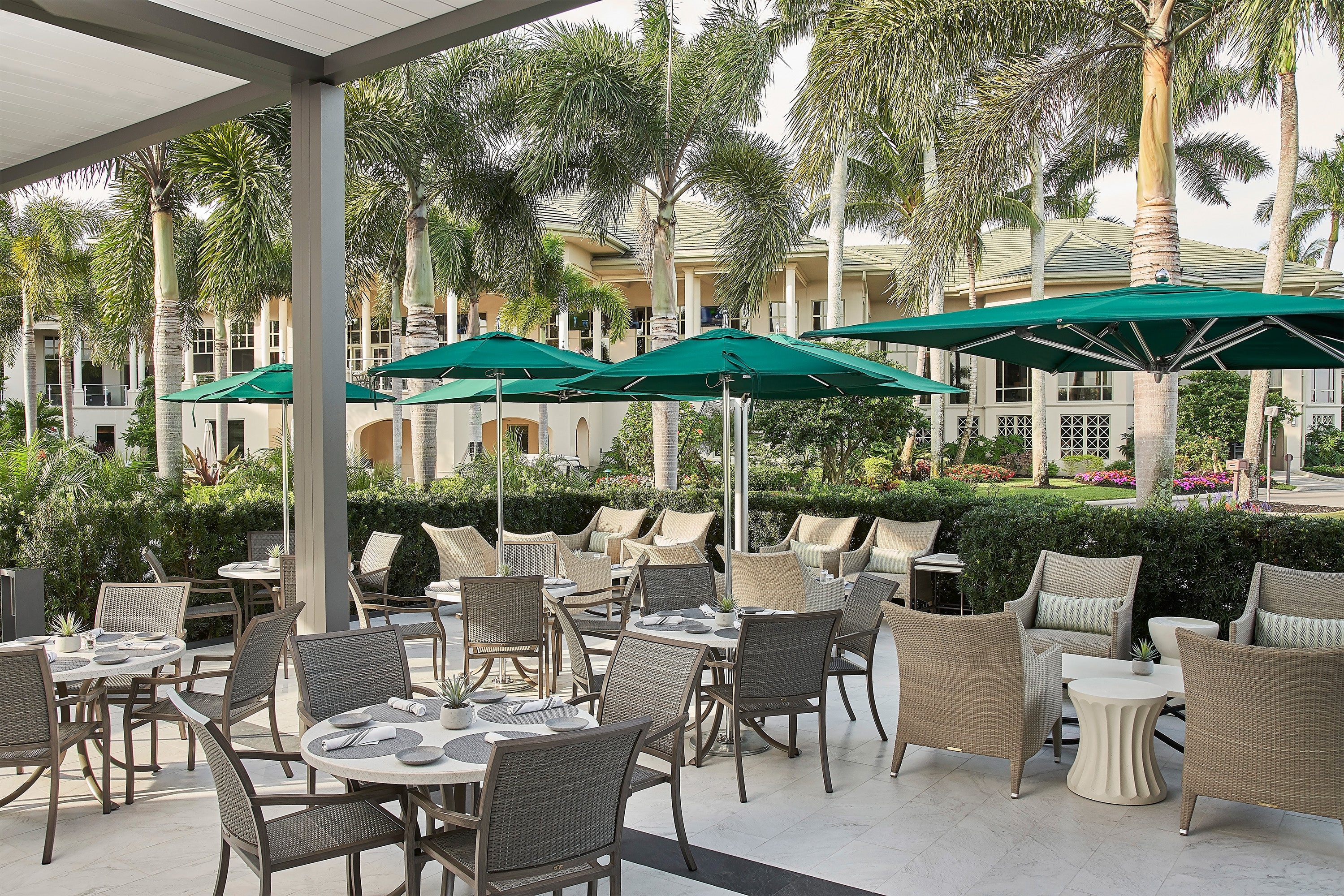 Outdoor dining area with tables, chairs, and green umbrellas under a clear sky.