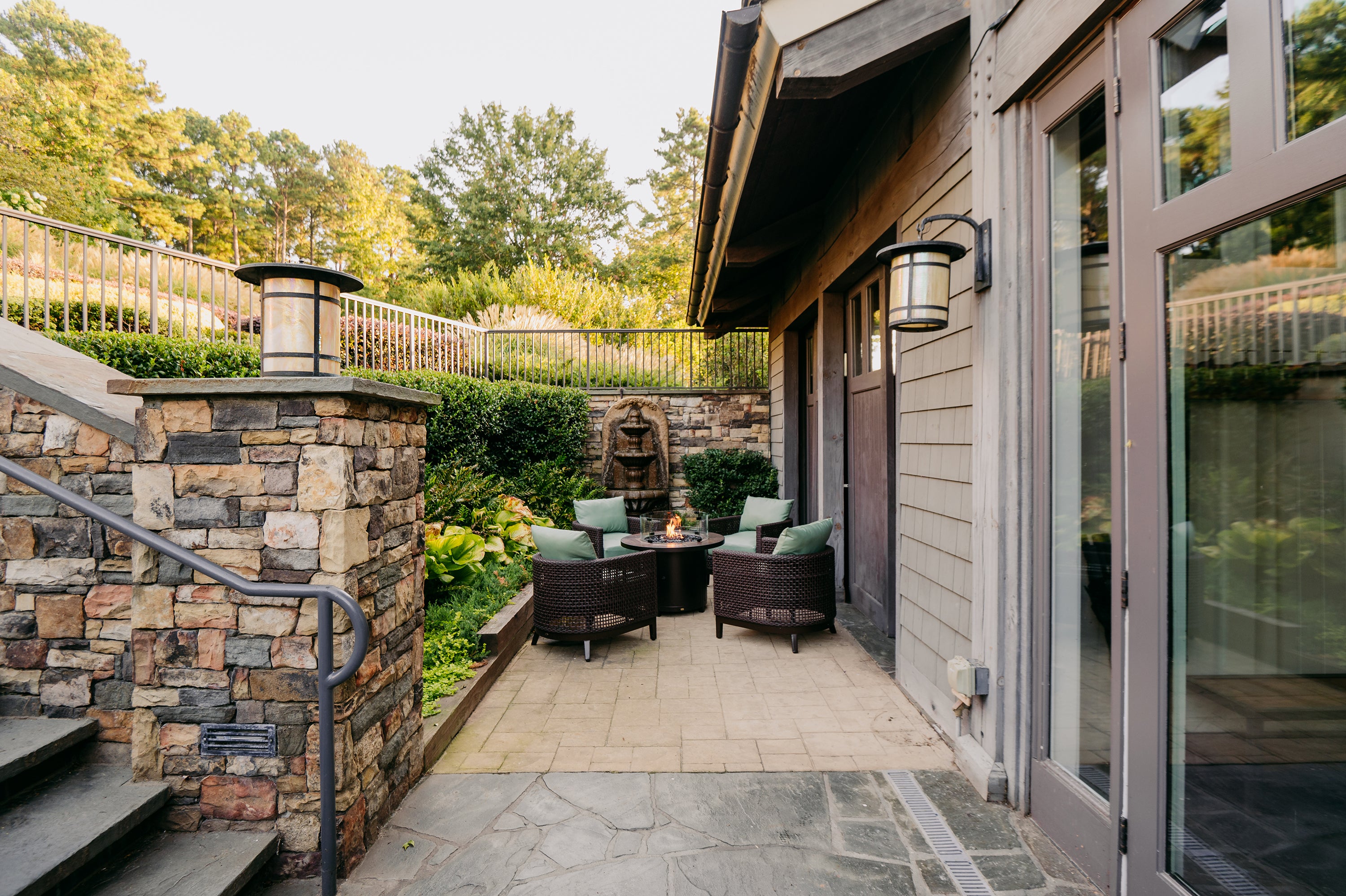 Outdoor patio area with stone wall, fire pit, and chairs near a house.