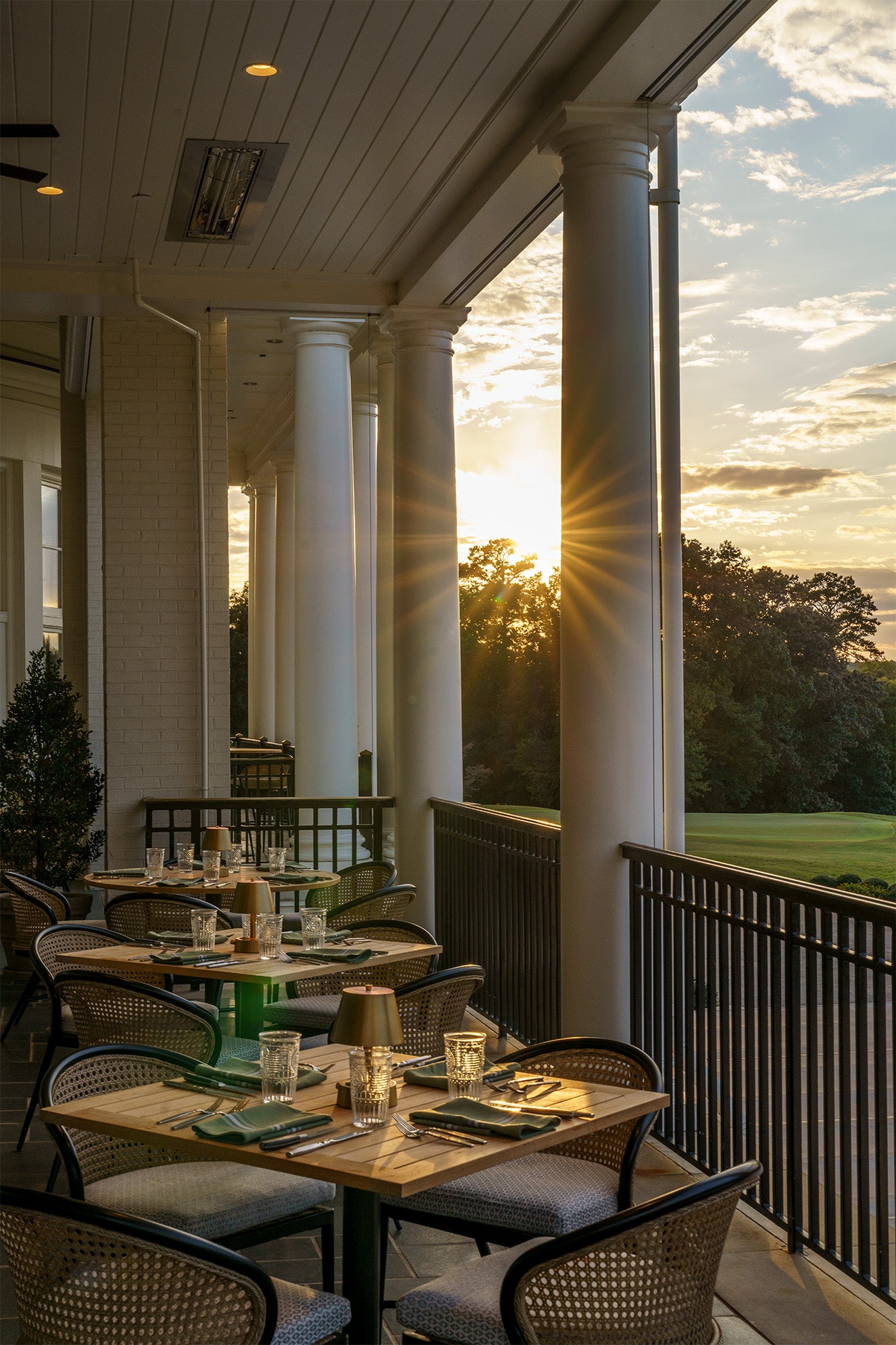 Outdoor dining area with tables and chairs on a porch during sunset.