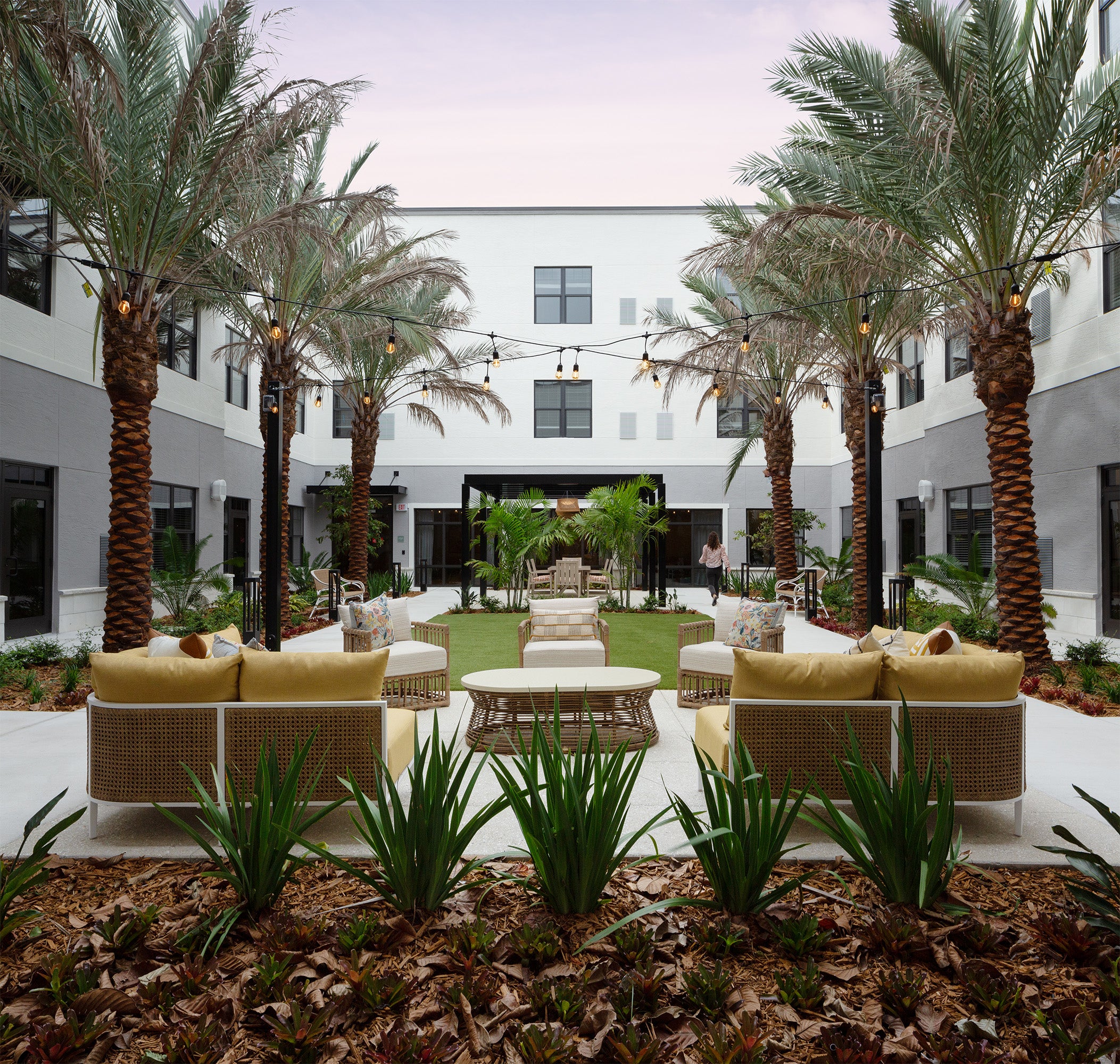 Outdoor senior living courtyard furnished with contract‑grade lounge seating, woven sofas, accent tables, and landscaped gathering space.